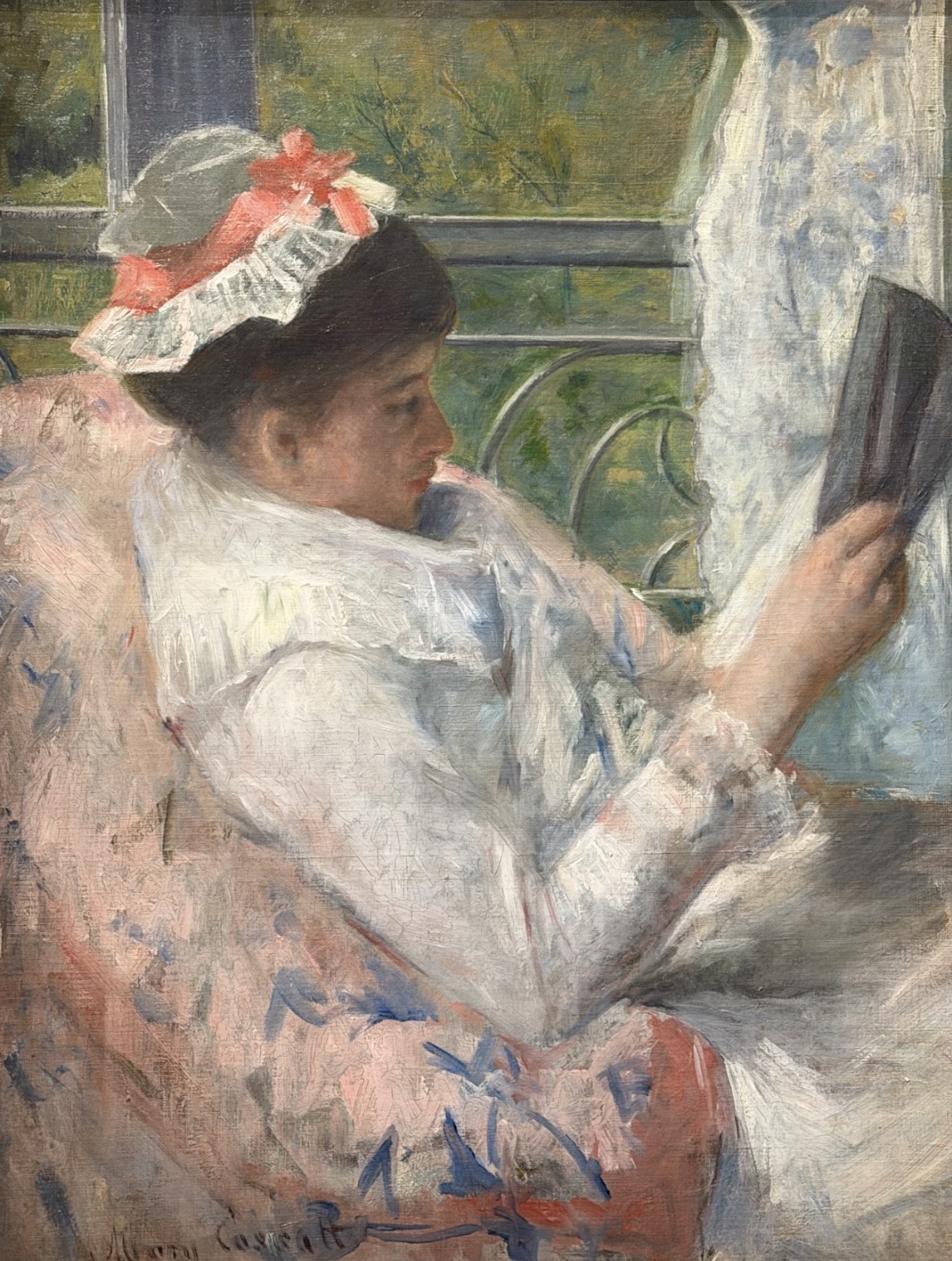 Mary Cassatt, Woman Reading: Lydia Cassatt in a white morning dress and lace cap with a coral bow reads in a floral armchair by a window.