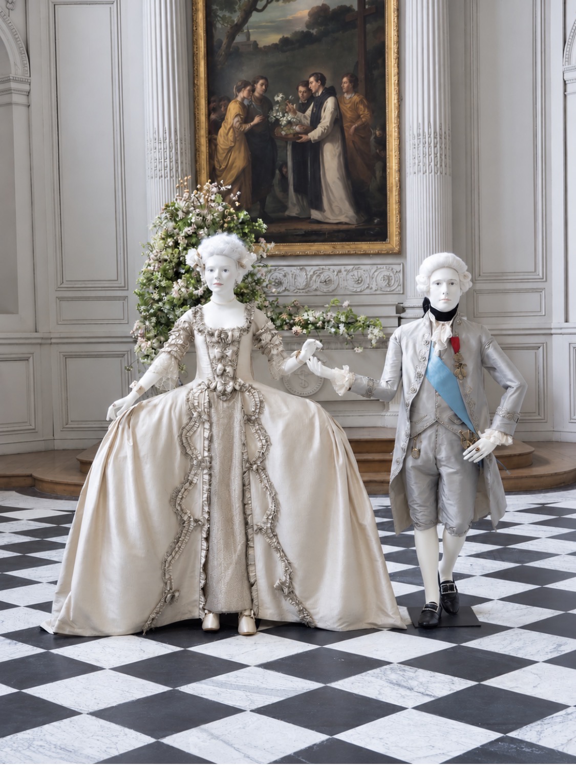 Milena Canonero’s court costumes for Marie Antoinette and Louis XVI, an ivory silk gown and a silver suit with a blue sash, at the Petit Trianon