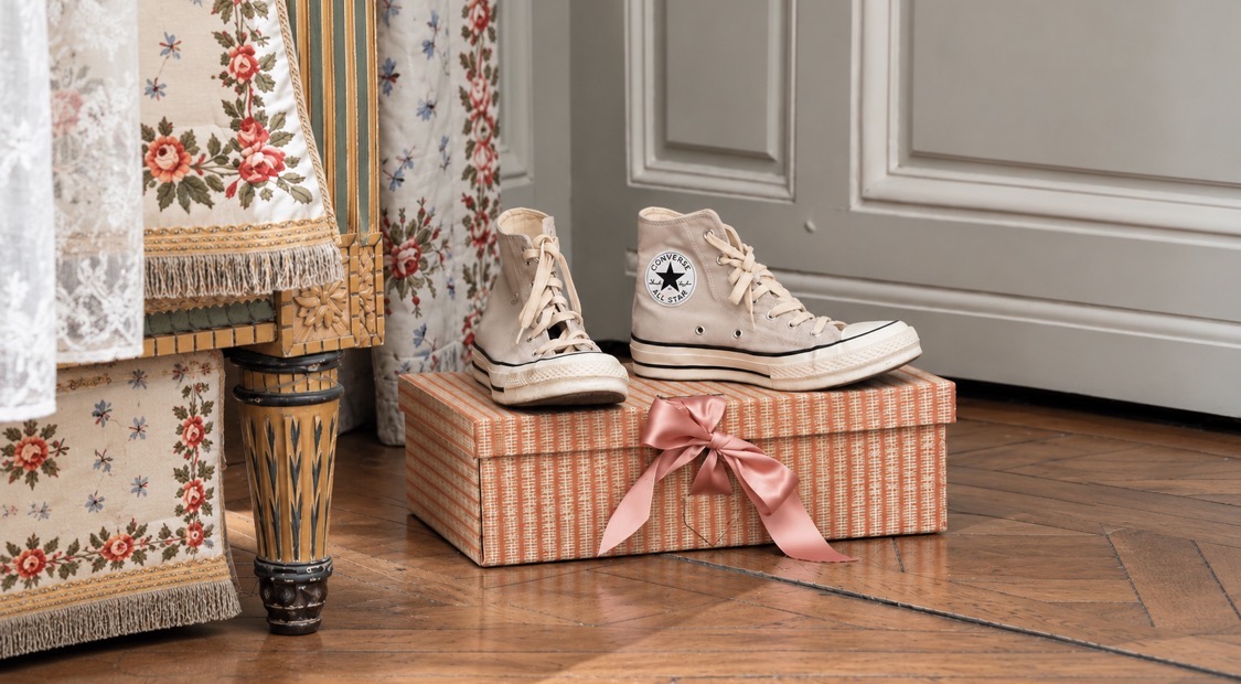Cream Converse high-tops on a pink striped shoebox tied with a satin bow at the Marie Antoinette exhibition, a nod to the film’s famous anachronism