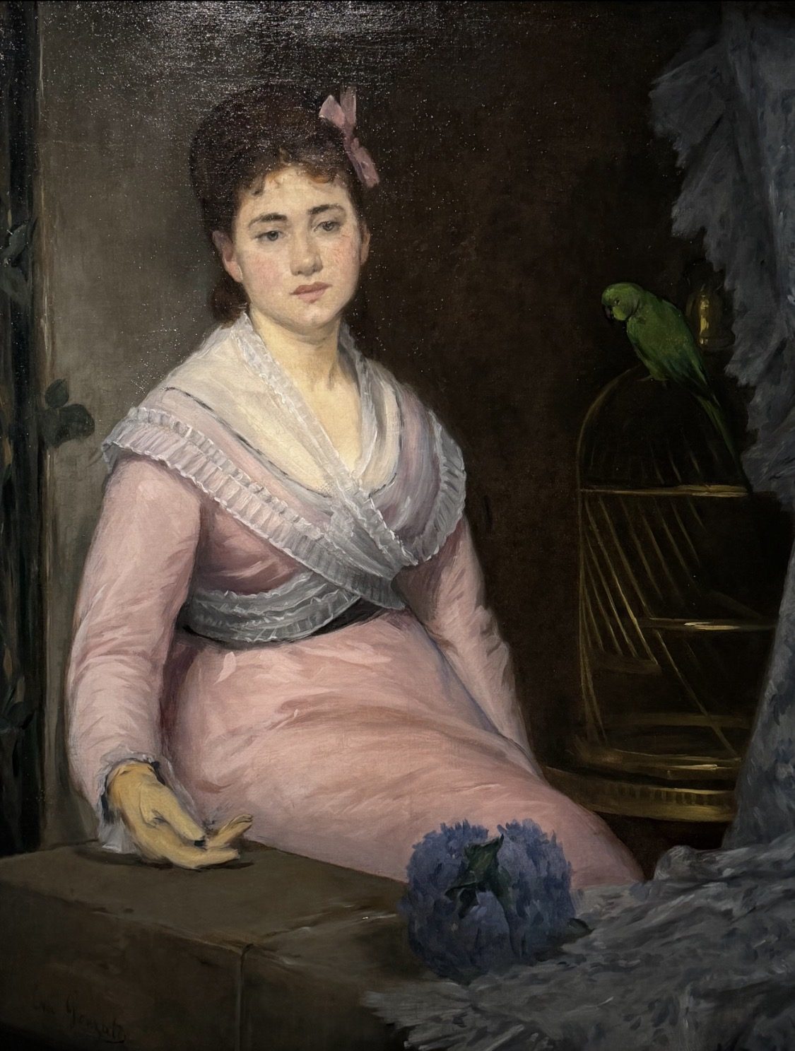Eva Gonzalès, L’Indolence: a young woman in a pink gown and one yellow glove sits beside a green parrot perched on its brass cage